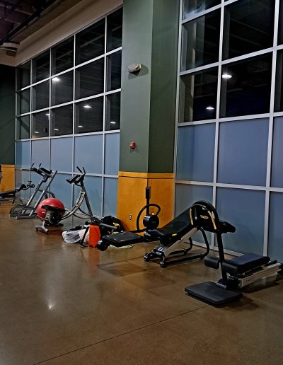 Interior view of inside gym with work out equipment in front of wall of windows with frosted windows on bottom