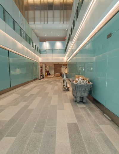 Interior view of brightly lit hallway with light blue walls, grey floors and glass windows