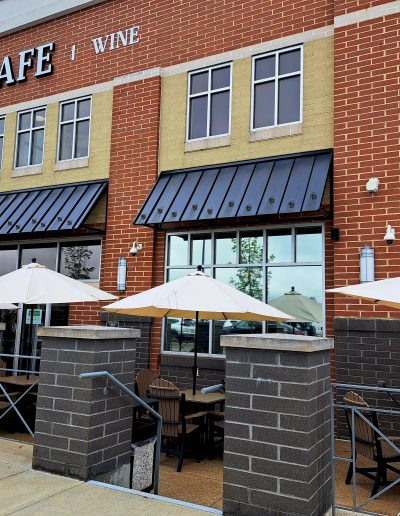 Outside view of brick café with black awnings, yellow umbrellas and seating in front of glass door and windows
