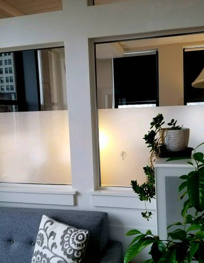 Interior view of office lobby wall with frosted windows with white wood framing and lamp with plants in front