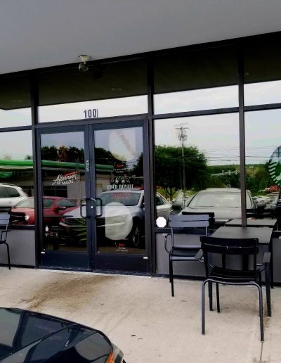 Front of Starbucks showing glass doors and rectangular windows framed in black reflecting parking lot