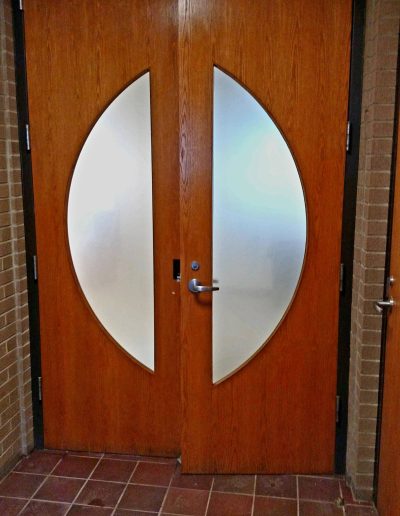 Long wooden office door with frosted glass inlays in brick wall