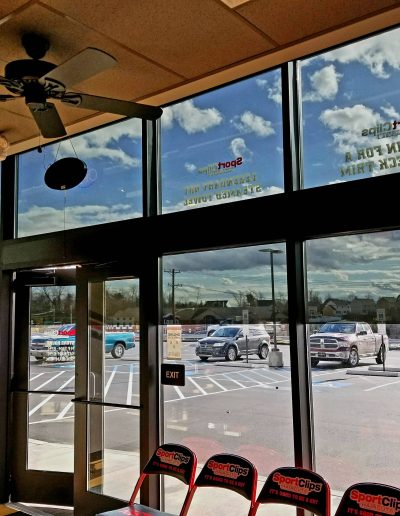 Interior view of front of SportClips location with large rectangular windows and glass door behind orange chairs