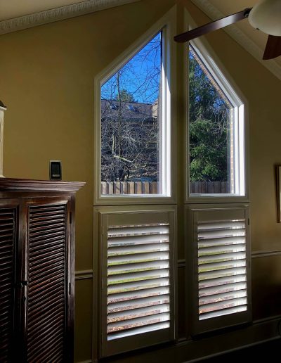 Interior view of pointed windows overlooking trees with slatted windows on bottom
