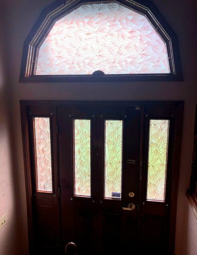 Wooden front door featuring frosted and etched decorative glass inserts with decorative window above
