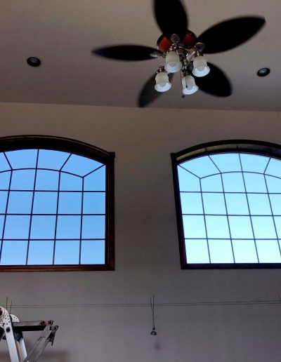 Interior view of home with vaulted ceilings and wooden ceiling fan in front of large curved divided square windows overlooking blue sky