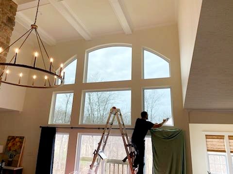 Man standing on ladder while cleaning large window divided into rectangles in living room