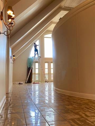 View of man standing on ladder cleaning large window in large home with tile floors