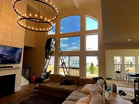 Man standing on ladder while cleaning large divided window in formal living room with black chandelier hanging