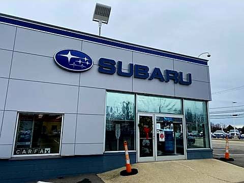Exterior view of Subaru location with blue sign, large windows and glass door by street